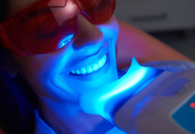 Woman in dental chair getting her teeth professionally whitened with a light