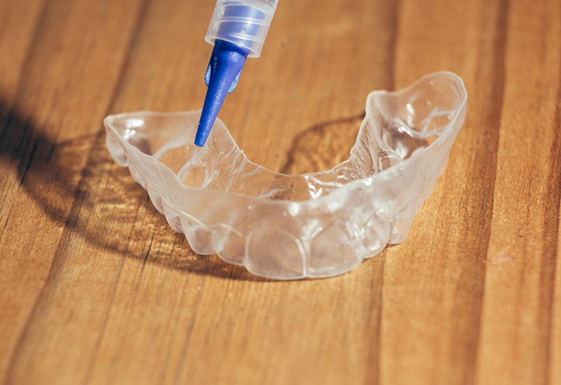 Applicator placing bleaching gel in clear teeth whitening tray