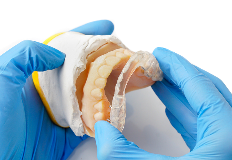 Dentist holding a model of the jaw and a clear tray to be worn over the teeth