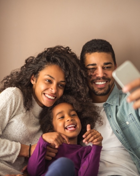 Mother and father taking selfie with their young daughter on couch