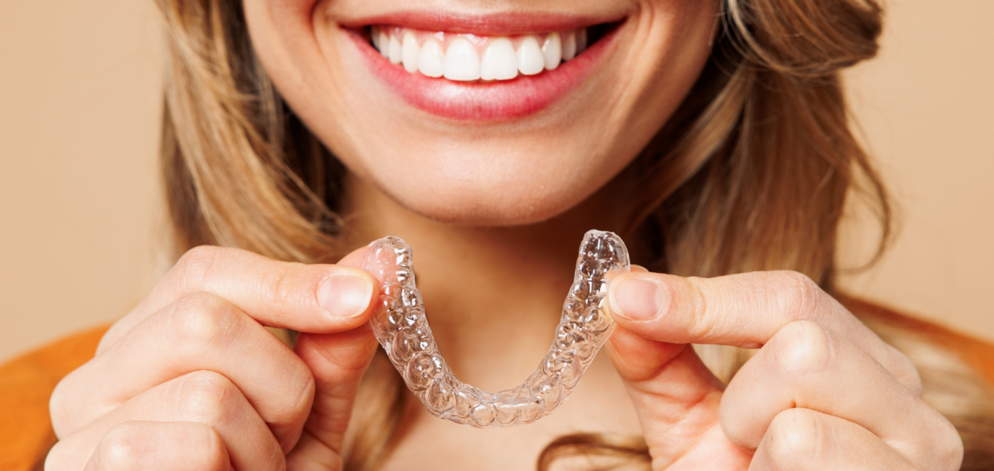 Close up of a smiling woman holding an Invisalign clear aligner in Wauwatosa