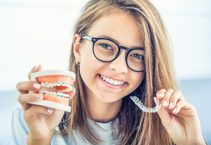 Young woman holding an Invisalign aligner and a model of the teeth with braces