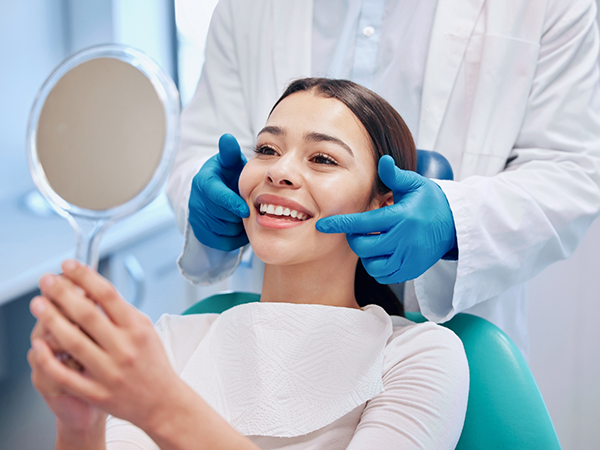 Woman in dental chair looking at her new smile in a mirror