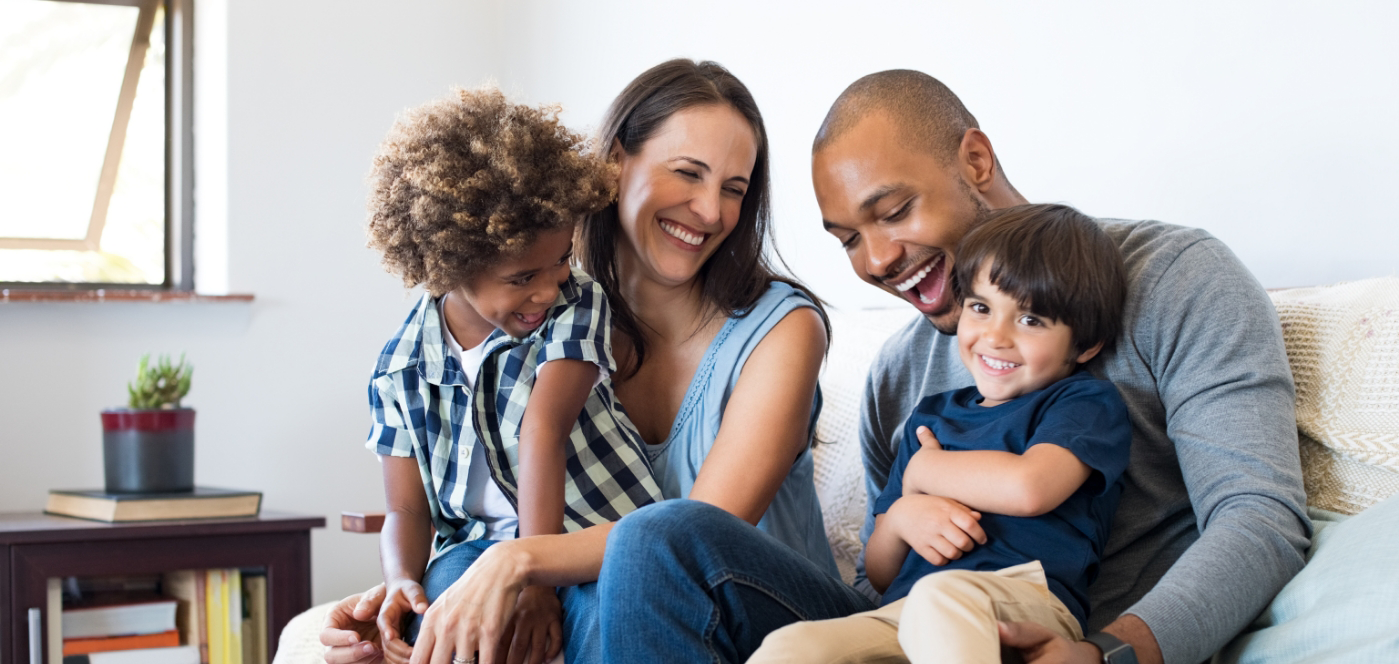 Family of four smiling on couch together after preventive dentistry checkups