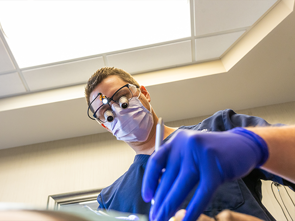 Dentist wearing dental binoculars and examining a patients mouth