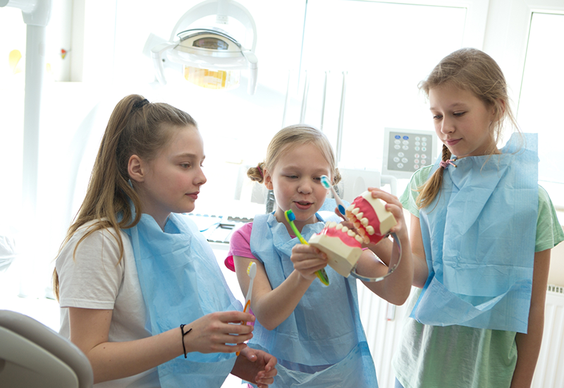 Three young girls in dental office holding toothbrushes and a model of the teeth