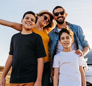 Family of four smiling outdoors on a sunny day