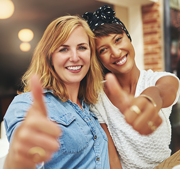 Two women smiling and giving thumbs up