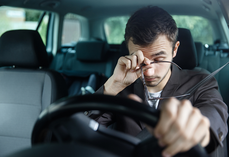 Tired man in drivers seat of car rubbing his eyes